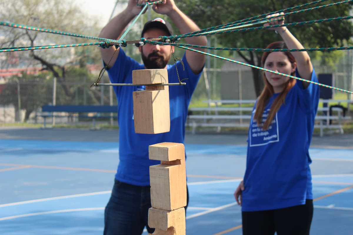 Participante de ALYAX sosteniendo una estructura de madera con cuerdas, representando la coordinación y el trabajo en equipo