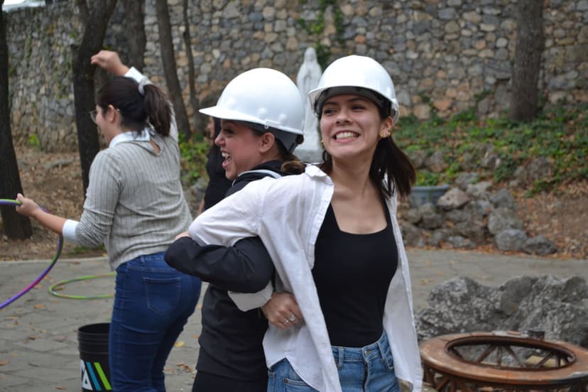 Dos mujeres usando cascos de seguridad durante una dinámica práctica, representando colaboración en contextos empresariales