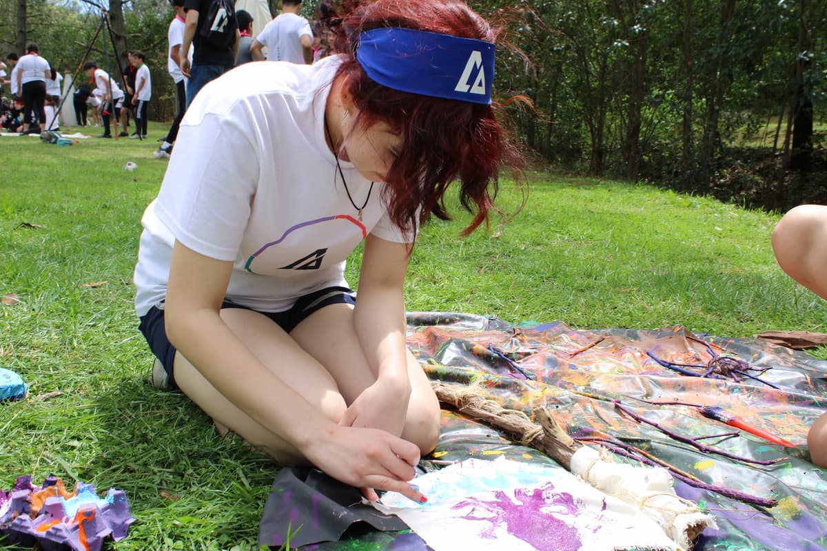 Joven participando en una actividad al aire libre, escribiendo en una libreta como parte de un ejercicio creativo en el campamento