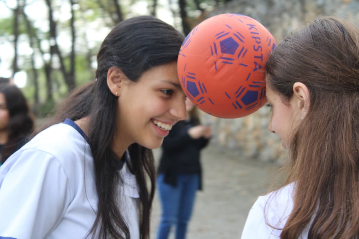 Alumna sosteniendo un balón mientras interactúa con sus compañeros, demostrando entusiasmo y cooperación